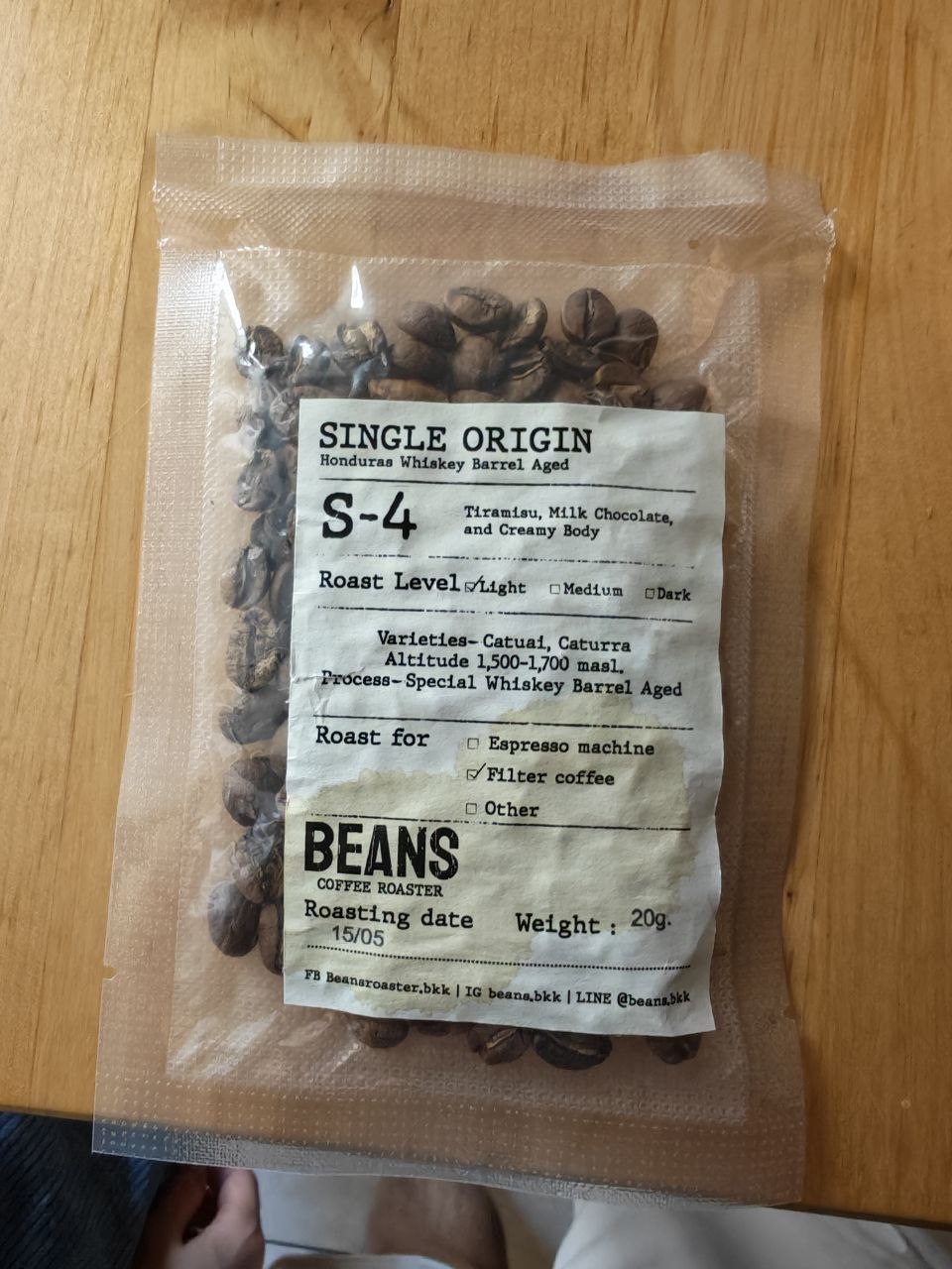 A 20-gram sample bag of light-roast Honduran whiskey-barrel-aged coffee beans from Beans Coffee Roaster on a wooden table.