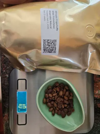 Ten grams of roasted coffee beans in a pale green dish on a digital scale beside a gold bag labeled Ethiopia Yirgacheffe Idido Yismashewa, anaerobic natural.